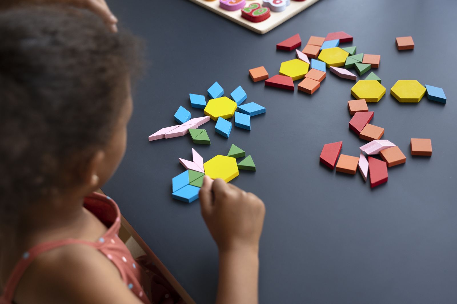 A child arranging coloured pattern blocks into flower shapes on a table