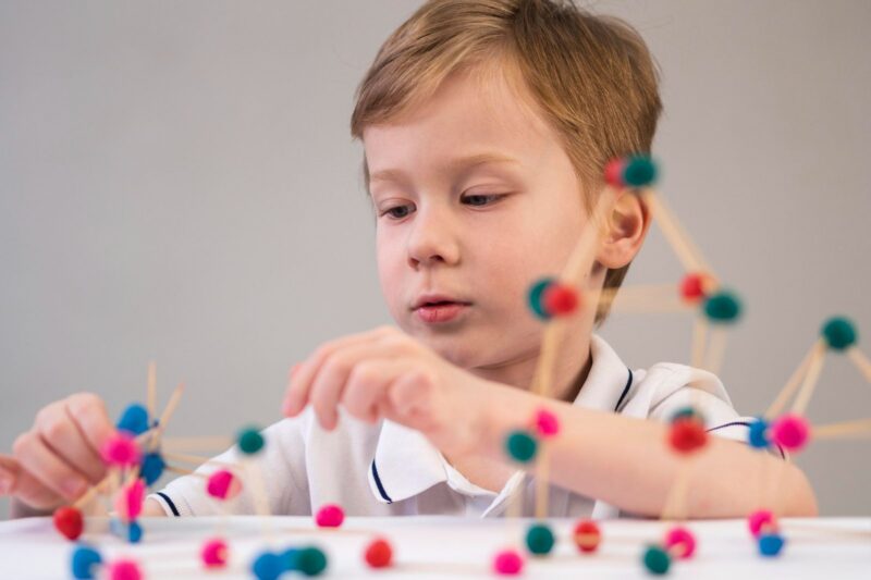 A boy concentrating as he builds a structure from sticks and pom-poms
