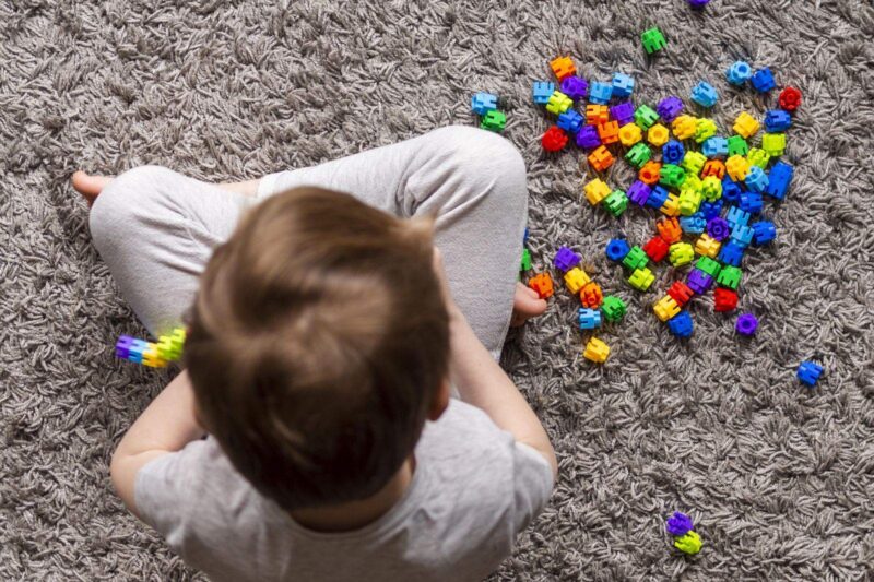 A child sitting on a carpet, sorting a pile of brightly coloured building bricks