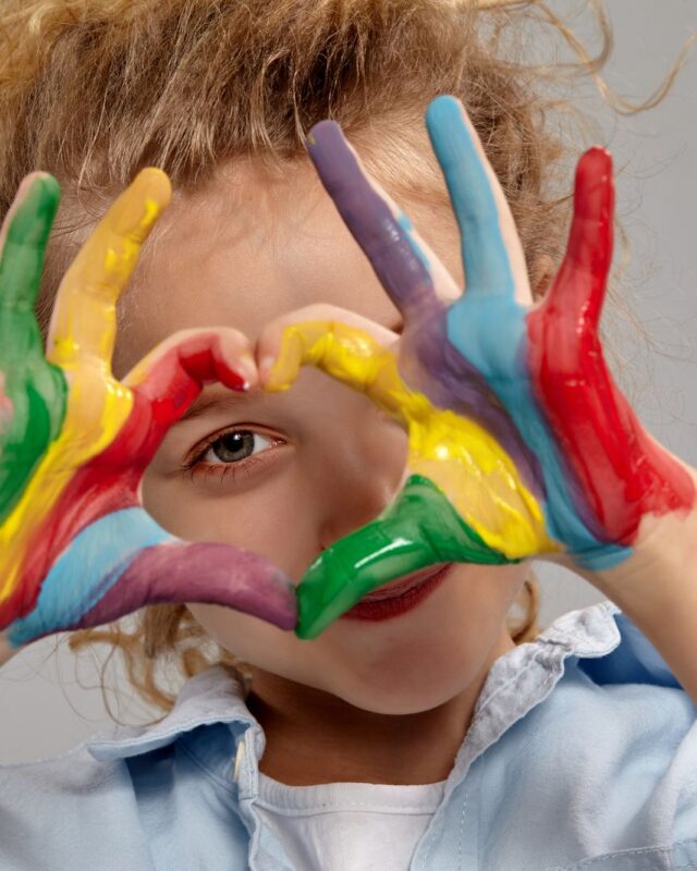 A child looking through their paint-covered hands, held in the shape of a heart