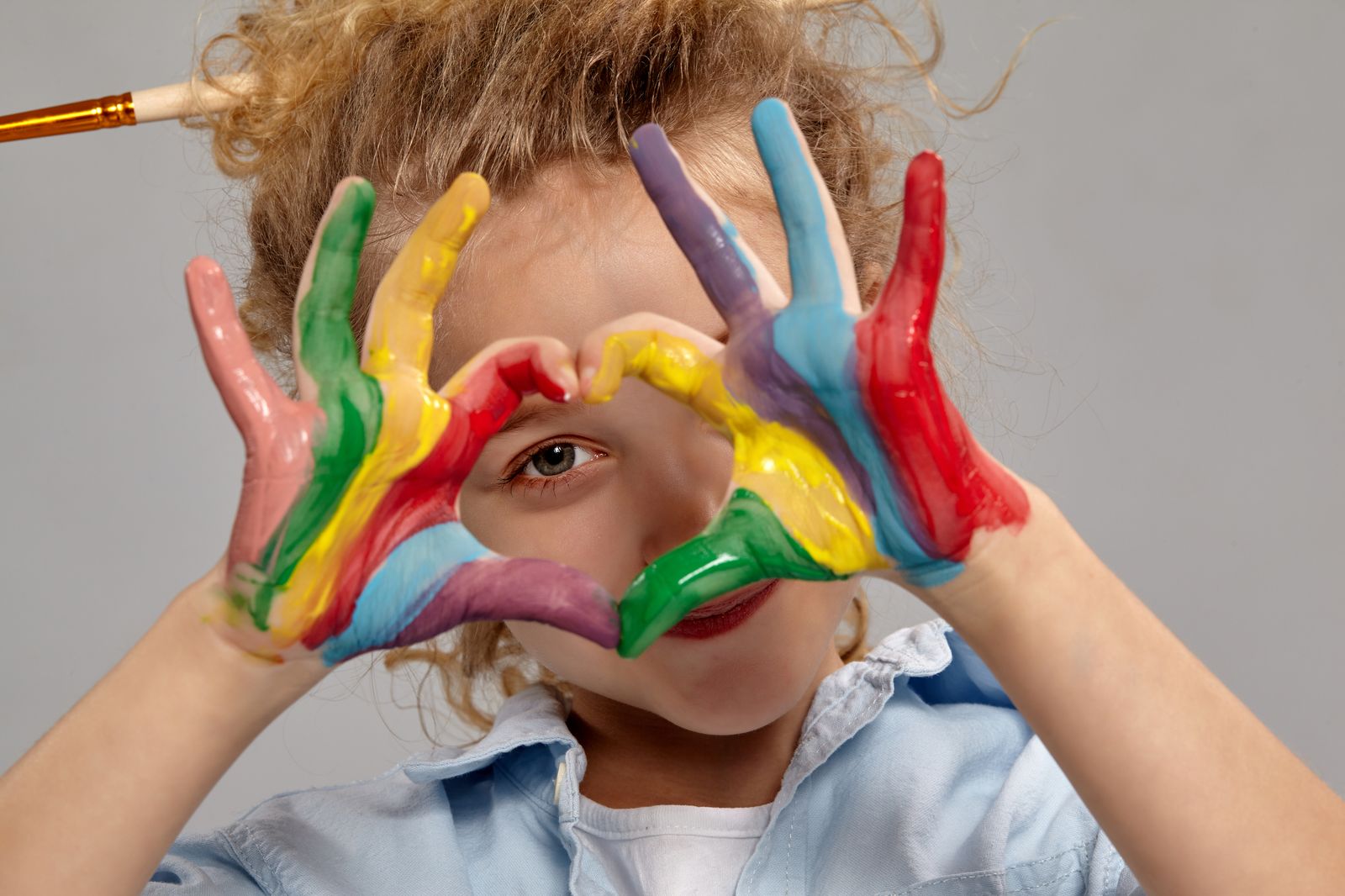 A child looking through their paint-covered hands, held in the shape of a heart